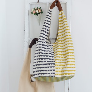 May include: Two fabric tote bags hanging on a white wooden frame. The bag on the left is a simple beige tote bag with the text "ithinksew.com" printed on the front. The bag on the right is a larger tote bag with a black and white geometric pattern on the left side and a yellow and white geometric pattern on the right side.