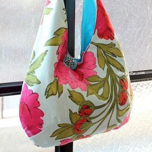 May include: A light blue tote bag with a floral print featuring pink flowers and green leaves. The bag has a turquoise blue strap.
