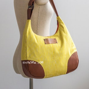 May include: A yellow and brown striped hobo bag with a brown leather trim and a brown leather strap. The bag has a zipper closure and a small leather patch with the text "ithinksew.com".