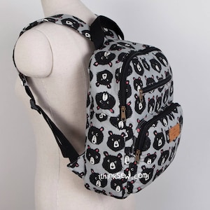 May include: A grey backpack with a black bear print. The backpack has two zipped compartments and adjustable straps.
