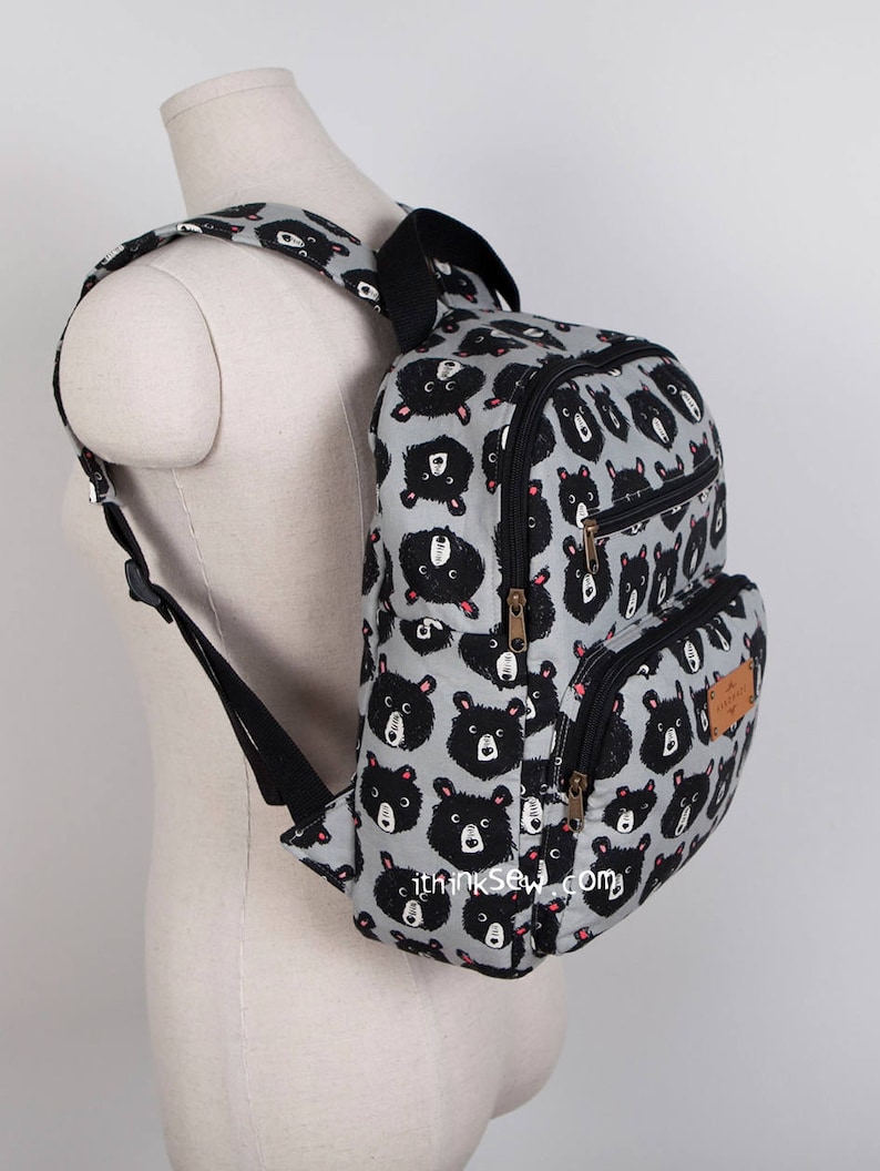 May include: A grey backpack with a black bear print. The backpack has two zipped compartments and adjustable straps.