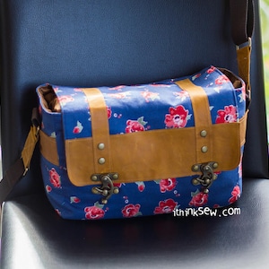 Pu&ograve; includere: Una borsa a tracolla in tela blu con una patta in pelle marrone e fibbie metalliche. La borsa ha una stampa floreale con fiori rossi e punti bianchi. La borsa ha una tracolla e il testo "thinksew.com" &egrave; stampato sul fondo.