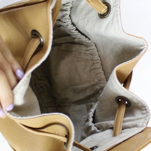 Peut inclure: L'int&eacute;rieur d'un sac seau en cuir brun avec une fermeture &agrave; cordon. Le sac est doubl&eacute; d'un tissu beige clair et poss&egrave;de une petite poche lat&eacute;rale.