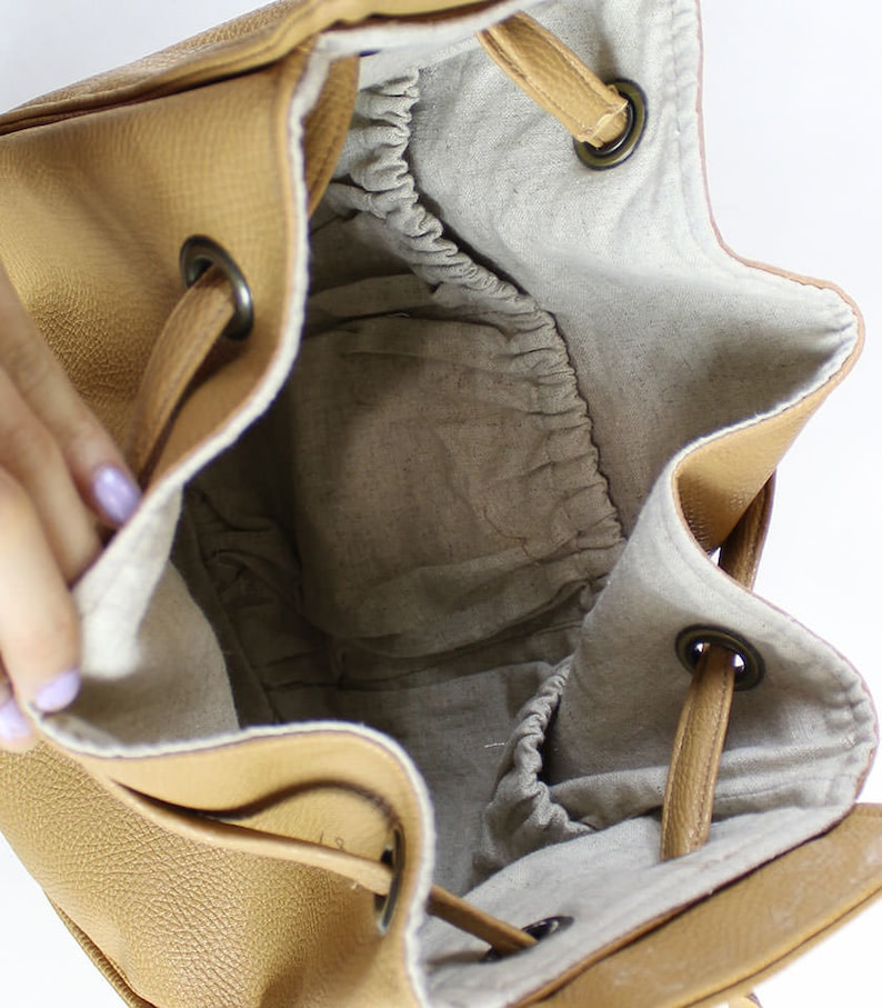 Peut inclure: L'int&eacute;rieur d'un sac seau en cuir brun avec une fermeture &agrave; cordon. Le sac est doubl&eacute; d'un tissu beige clair et poss&egrave;de une petite poche lat&eacute;rale.