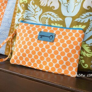 K&ouml;nnte beinhalten: Eine kleine orangefarbene und wei&szlig;e Clutch mit Punkten, blauem Besatz und einem schl&uuml;sself&ouml;rmigen Metallakzent. Die Clutch hat einen langen Riemen und der Text "ithinksew.com" ist in der rechten unteren Ecke sichtbar.