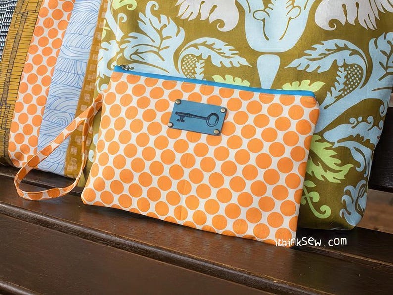 K&ouml;nnte beinhalten: Eine kleine orangefarbene und wei&szlig;e Clutch mit Punkten, blauem Besatz und einem schl&uuml;sself&ouml;rmigen Metallakzent. Die Clutch hat einen langen Riemen und der Text "ithinksew.com" ist in der rechten unteren Ecke sichtbar.
