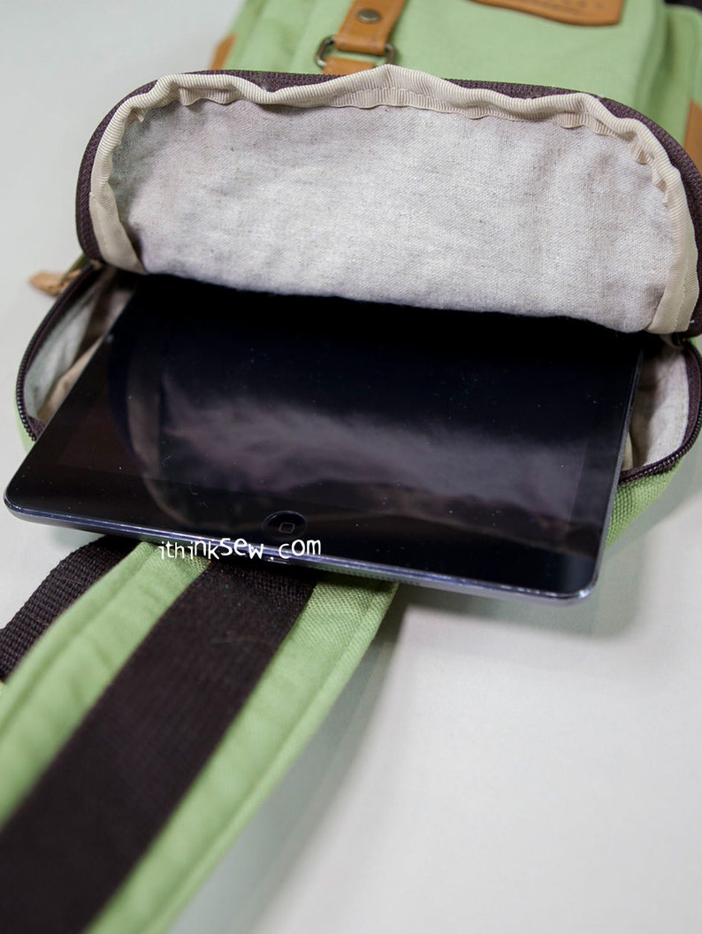 May include: A light green canvas sling bag with brown accents and a dark brown strap, featuring an open zippered compartment containing a black tablet. The text ithinksew.com is printed in white on the surface of the black tablet screen.
