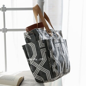 May include: A large gray and white geometric patterned tote bag with brown leather handles. The bag has multiple pockets and a zipper closure.