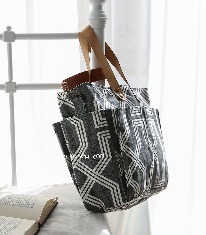 May include: A large gray and white geometric patterned tote bag with brown leather handles. The bag has multiple pockets and a zipper closure.