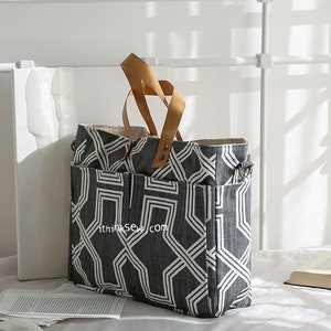 May include: A large black and white geometric patterned tote bag with brown leather handles. The bag has multiple pockets and a zipper closure.