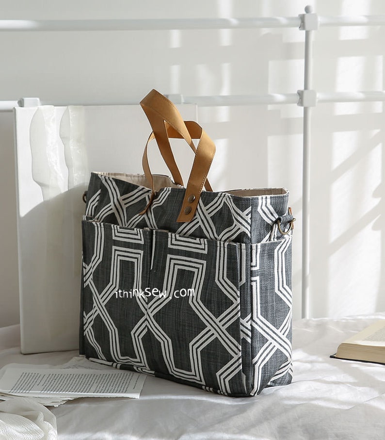 May include: A large black and white geometric patterned tote bag with brown leather handles. The bag has multiple pockets and a zipper closure.