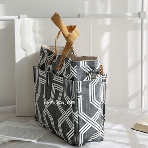 May include: A large gray and white geometric patterned tote bag with brown leather handles. The bag has multiple pockets and a zipper closure.
