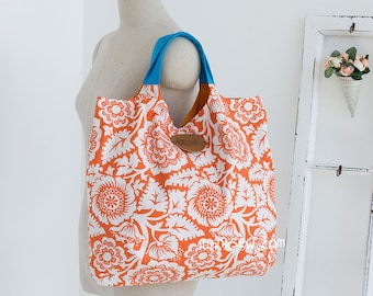 May include: A large orange and white floral tote bag with a blue handle. The bag is made of fabric and has a brown leather tag.