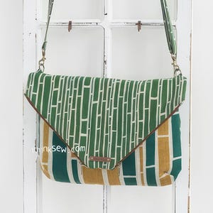 May include: A green and yellow fabric crossbody bag with a brown leather flap and strap. The bag has a geometric pattern and the text "thinksew.com" is printed on the front.