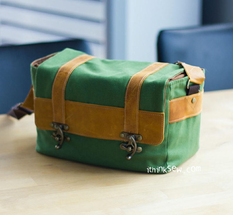 Pu&ograve; includere: Una borsa per fotocamera in tela verde con dettagli in pelle marrone e fibbie metalliche. La borsa ha una tracolla ed &egrave; realizzata con materiali resistenti.
