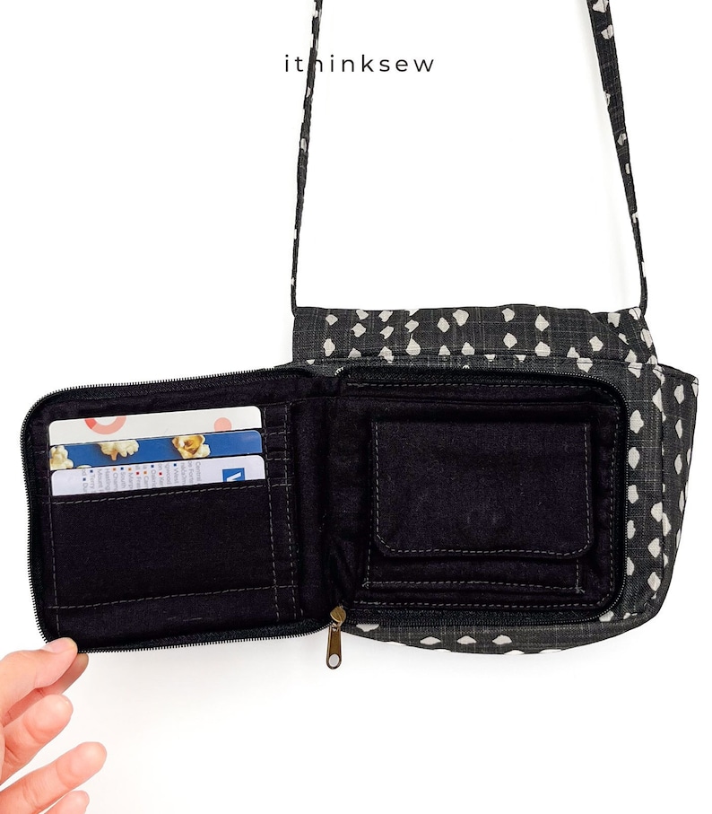 May include: A black and white patterned crossbody bag with a zippered closure. The bag is open and shows a black interior with multiple pockets and card slots. The bag is made of fabric and has a black strap.