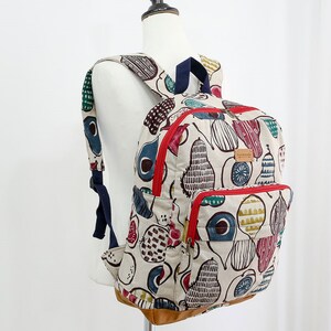May include: A beige canvas backpack with a red zipper and a brown leather bottom. The backpack is decorated with a colorful pear pattern and the word "handmade" is printed on the front.