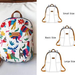 Può includere: Uno zaino bianco con un design ricamato colorato con uccelli, fiori e cervi. Lo zaino ha spallacci in pelle marrone e una piccola tasca frontale. La parola "handmade" è su una piccola etichetta in pelle marrone. L'immagine mostra anche tre opzioni di dimensioni dello zaino.