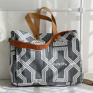 May include: A gray and white geometric patterned tote bag with brown leather straps and handles. The bag has a zipper closure and a small pocket on the front. The text "thinksew.com" is printed on the front of the bag.