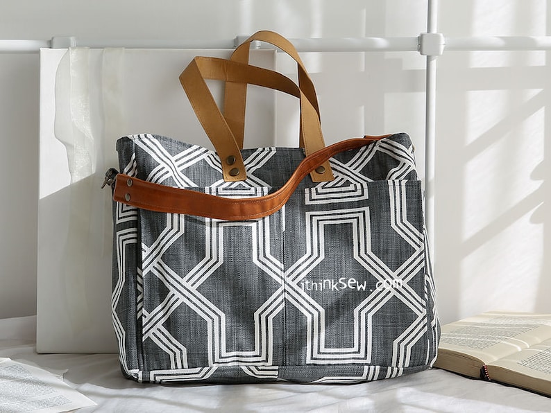 May include: A gray and white geometric patterned tote bag with brown leather straps and handles. The bag has a zipper closure and a small pocket on the front. The text "thinksew.com" is printed on the front of the bag.