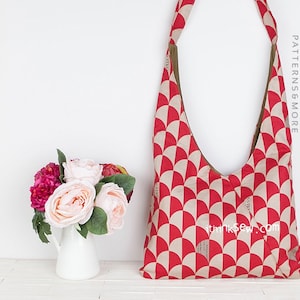 Op de afbeelding: Een stoffen schoudertas met een rood en beige geometrisch patroon. De tas heeft een lange band en wordt gepresenteerd tegen een witte achtergrond. Links staat een boeket roze en perzik bloemen in een witte kan. De tekst "ithinksew PATTERNS&MORE" is zichtbaar.