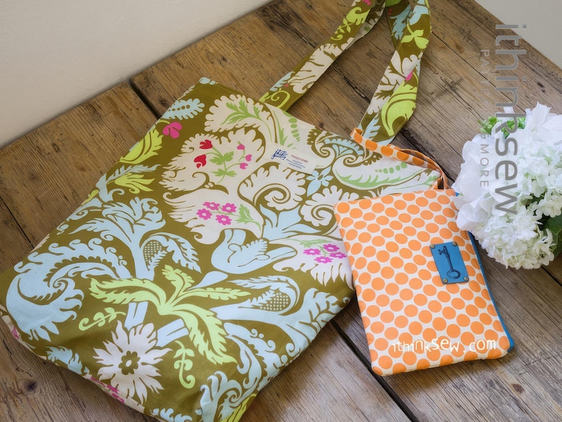 K&ouml;nnte beinhalten: Eine gr&uuml;ne und blaue Blumentasche mit einer kleineren orangefarbenen Tasche mit Punkten. Die Tasche hat einen blauen Schl&uuml;sselanh&auml;nger. Die Tasche hat ein wei&szlig;es Etikett mit dem Text "thinksew more" darauf.