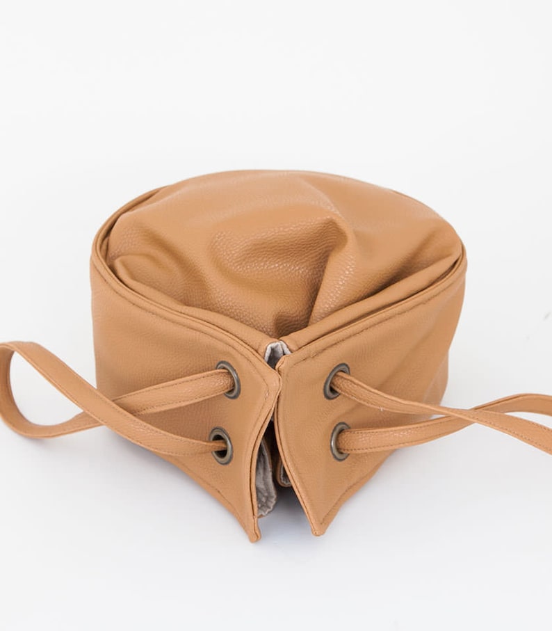 Peut inclure: Un sac seau en cuir brun avec une fermeture &agrave; cordon et deux anses. Le sac a une finition en cuir textur&eacute; et des &oelig;illets m&eacute;talliques.