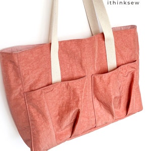 May include: A coral-colored tote bag with two large pockets on the front and two white canvas straps. The bag is made of a lightweight, water-resistant fabric.