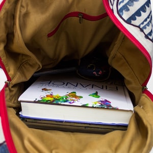 May include: A brown canvas backpack with a red zipper and a blue and white patterned design. The backpack is open and filled with books, including one titled "Introduction to Corporate Finance".