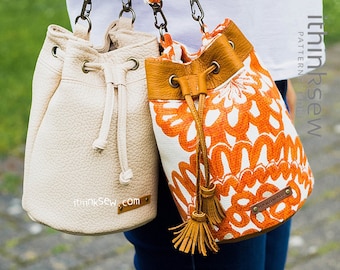 Peut inclure: Deux sacs seau, l'un est blanc avec une garniture en cuir marron et l'autre est blanc avec un motif floral orange. Les deux sacs ont une fermeture à cordon et un pompon en cuir marron.