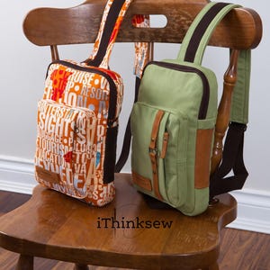 May include: Two sling backpacks with single shoulder straps. One bag features an orange fabric with white text including words like cruise, trip, and resort. The other bag is solid sage green with brown leather-like accents and a front buckle strap.