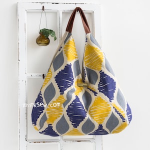 May include: A large, yellow, blue, and gray tote bag with a geometric pattern. The bag has brown leather handles and a small metal tag.