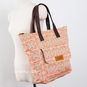 May include: A large orange and blue geometric patterned tote bag with brown leather handles. The bag has a smaller pocket on the front with a brown leather label that says "Barista".