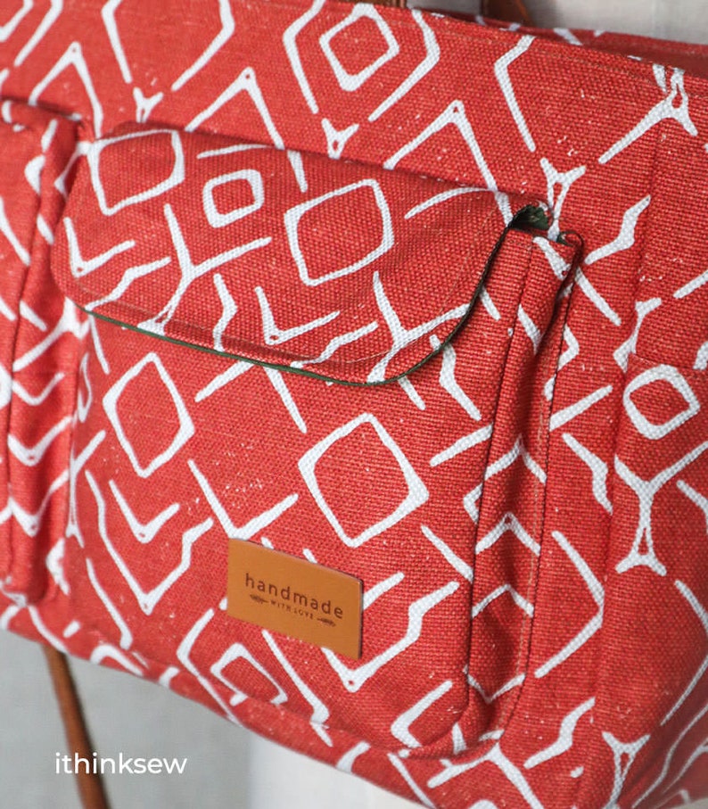 K&ouml;nnte beinhalten: Rote Canvas-Tragetasche mit wei&szlig;em geometrischem Muster und einem braunen Leder-Patch mit der Aufschrift "handmade with love".