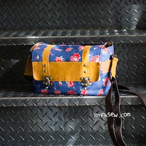 Pu&ograve; includere: Una borsa a tracolla in tela blu con una patta in pelle marrone e dettagli in metallo. La borsa ha un motivo floreale e una lunga tracolla regolabile. La borsa &egrave; appoggiata su una superficie metallica. thinksew.com