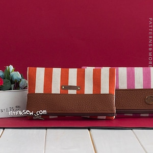 May include: Two striped fabric zippered pouches with brown leather accents. The pouch on the left has orange and white stripes, and the pouch on the right has pink and white stripes.