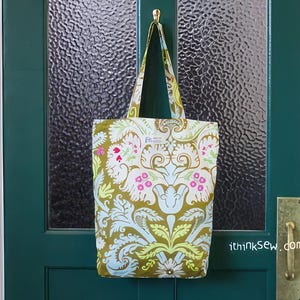 K&ouml;nnte beinhalten: Eine gr&uuml;n-wei&szlig;e Einkaufstasche mit Blumenmuster h&auml;ngt an einer gr&uuml;nen T&uuml;r. Die Tasche hat einen goldenen Henkel und ein wei&szlig;es Etikett mit dem Text "ithinksew.com".