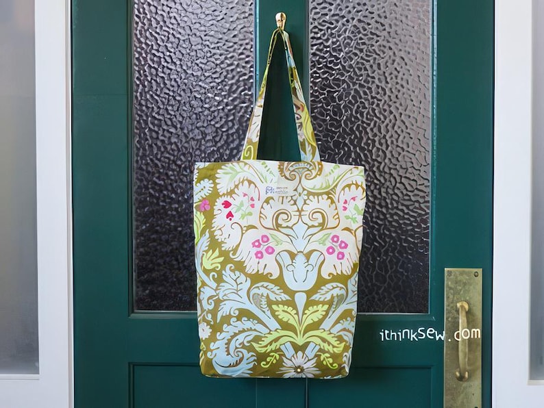 K&ouml;nnte beinhalten: Eine gr&uuml;n-wei&szlig;e Einkaufstasche mit Blumenmuster h&auml;ngt an einer gr&uuml;nen T&uuml;r. Die Tasche hat einen goldenen Henkel und ein wei&szlig;es Etikett mit dem Text "ithinksew.com".