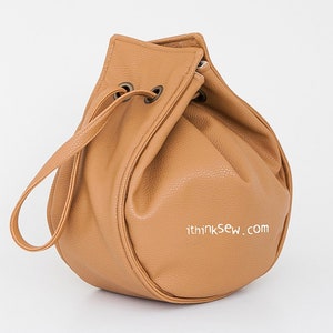 Peut inclure: Un sac seau en cuir brun clair avec une seule sangle. Le sac a une forme ronde et est fait d'un cuir souple et textur&eacute;. Le sac a une adresse de site Web imprim&eacute;e sur le fond : "ithinksew.com".