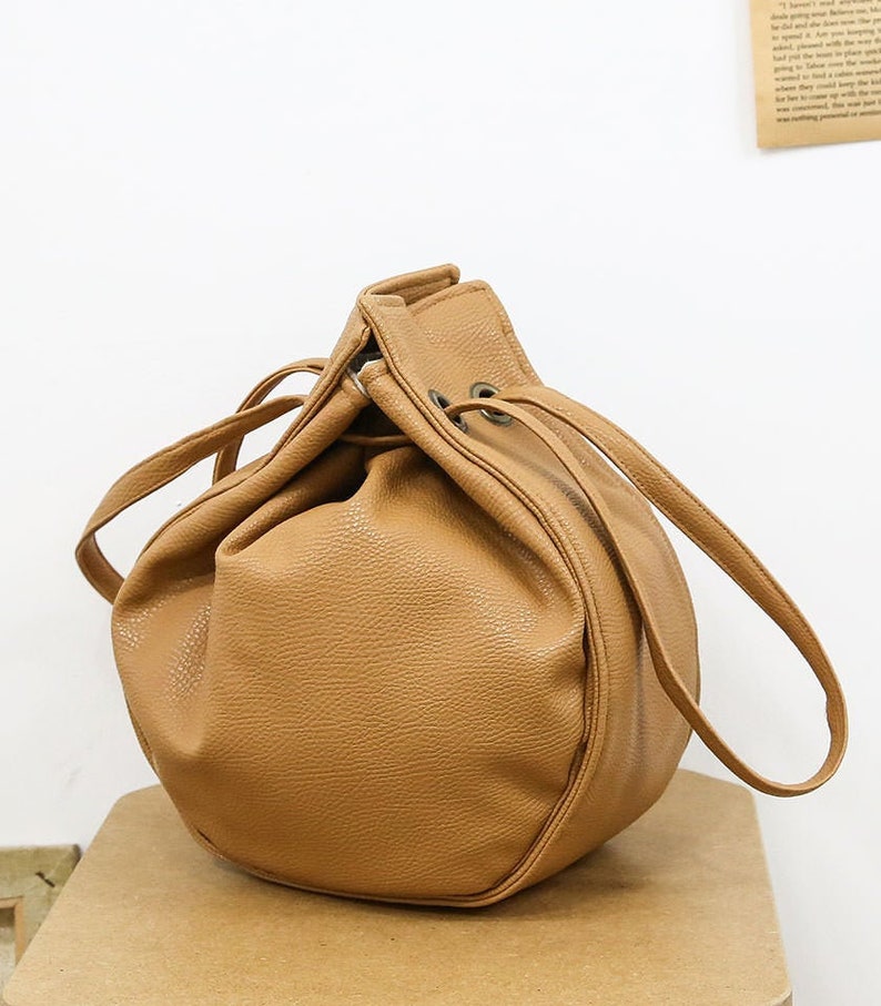 Peut inclure: Un sac seau en similicuir marron avec une fermeture &agrave; cordon et deux anses.