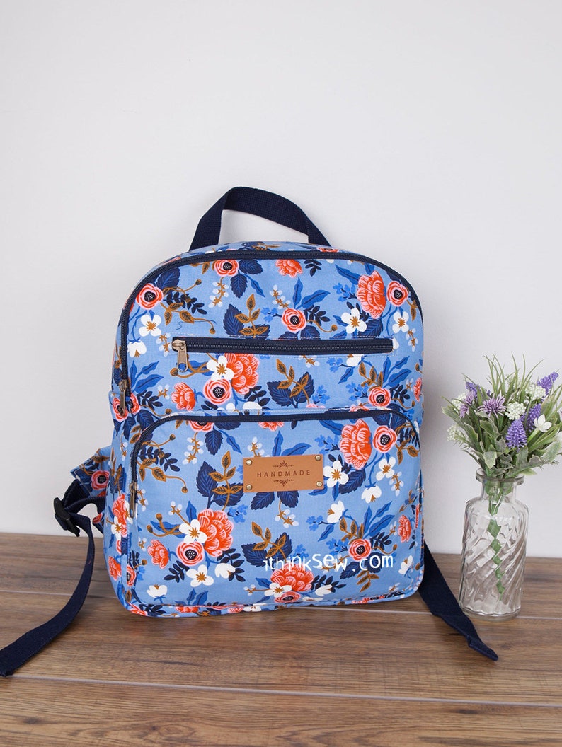 May include: A blue floral backpack with navy blue straps and a brown leather patch that says "Handmade with Love".