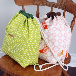 May include: Two drawstring backpacks with rope straps. The left bag is lime green with a white geometric pattern and a dark green top. The right bag is light pink with a white clover pattern, orange octopus illustrations, and a brown top.