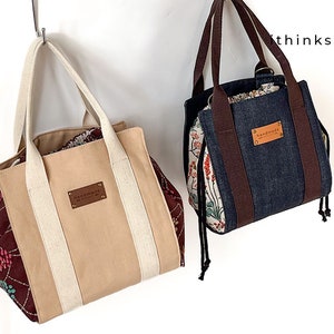 Może przedstawiać: Dwie ręcznie robione torby typu tote z kwiatowego materiału i dżinsu. Obie torby mają brązowe skórzane paski i brązową skórzaną metkę z napisem "ręcznie robione".