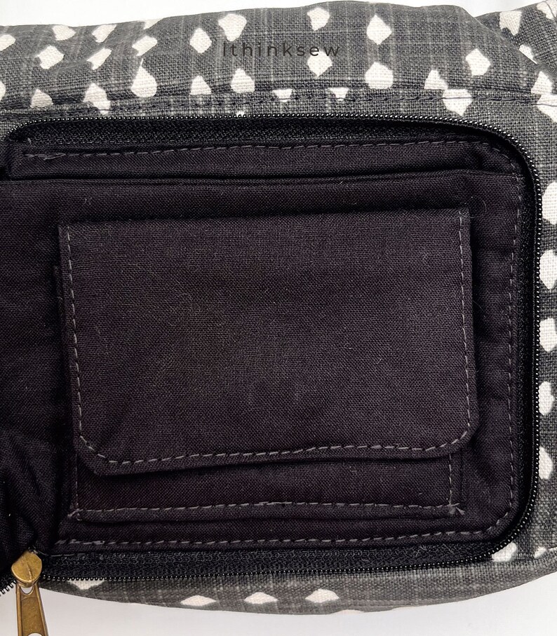 May include: Close-up of a gray and white patterned fanny pack with a black interior pocket. The fanny pack has a zipper closure and a small pocket inside. The text "ithinksew" is printed on the top of the fanny pack.