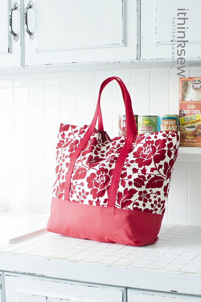 May include: A red and white floral tote bag with red handles. The bag is sitting on a white tiled counter.