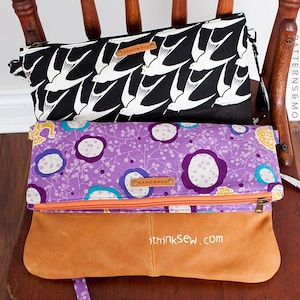 May include: Three fabric clutches with different patterns. The top clutch has a black and white pattern of birds. The middle clutch has a purple background with white and purple flowers. The bottom clutch is brown leather. All three clutches have a "Handmade" label.