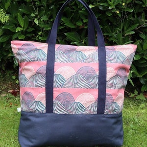May include: A large tote bag with navy blue straps and a pink and green geometric pattern. The bag has a solid navy blue bottom.