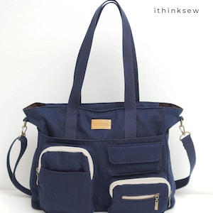 May include: Navy blue tote bag with multiple exterior pockets and a shoulder strap. The bag has a rectangular shape with a top handle and a small gold-colored tag that says "handmade". The text "ithinksew" is in the upper right corner.