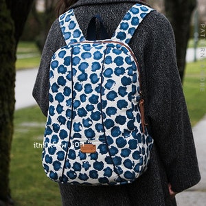 Pode incluir: Uma mochila azul e branca com padrão e detalhes em couro marrom. A mochila tem fecho de correr e alças ajustáveis.