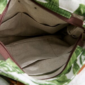 May include: The inside of a green and white tote bag with a brown zipper and a brown fabric lining. The bag has a small pocket on the inside.